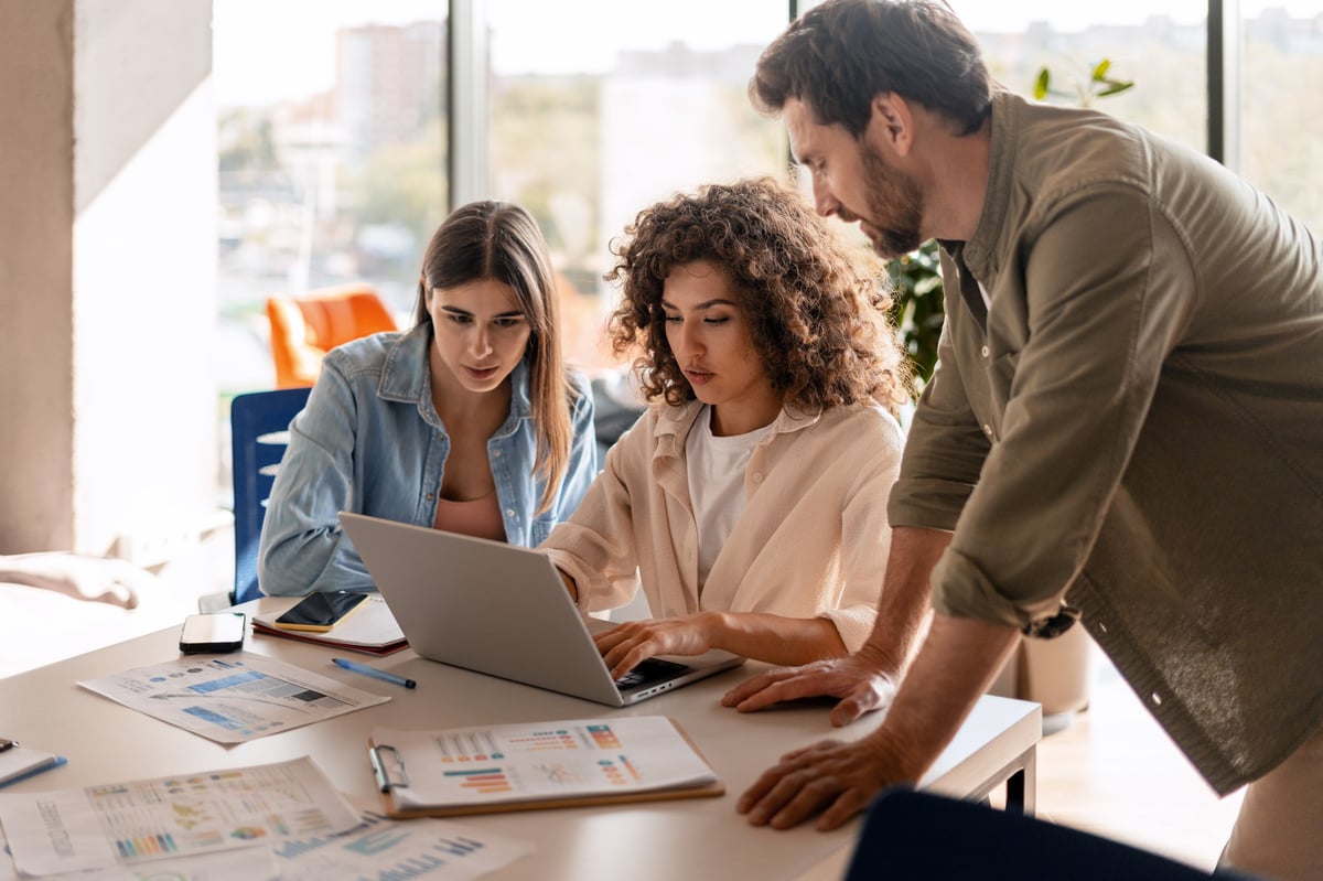 Three colleagues collaborating on a project over a laptop in a modern office